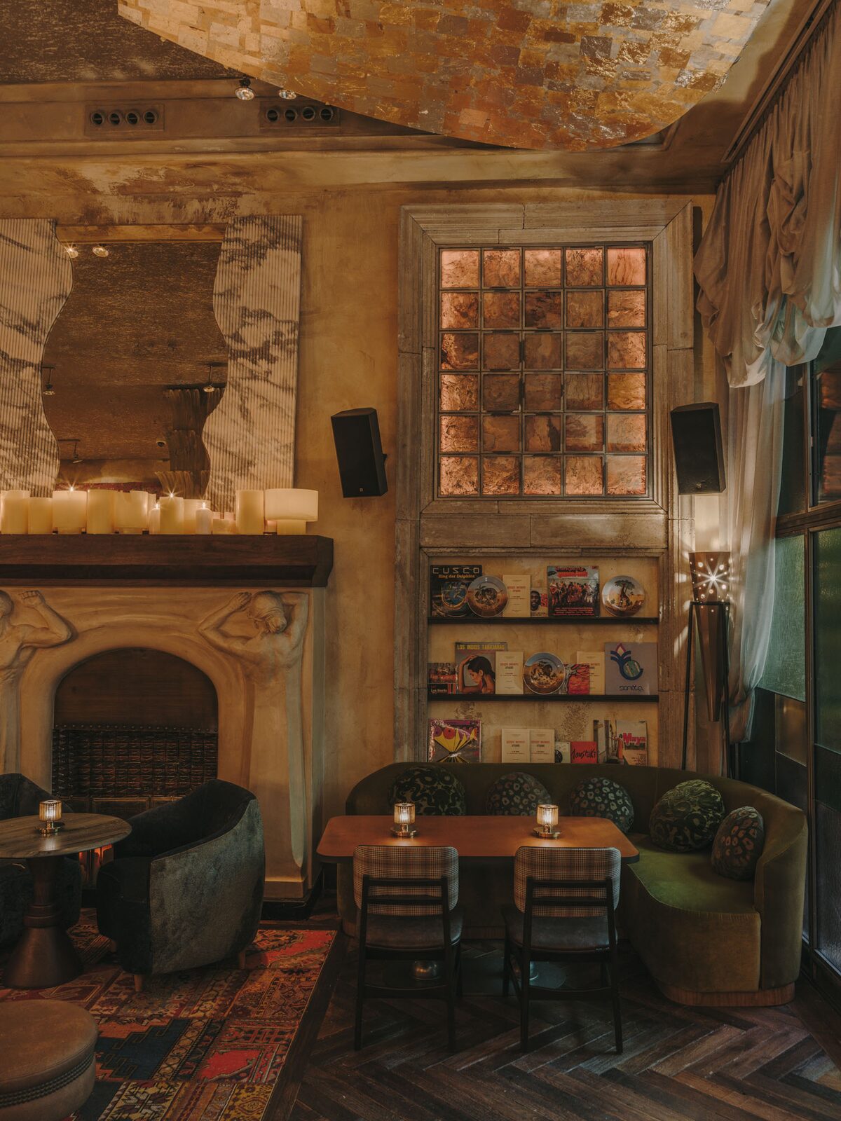 Salón de 61 con chimenea de figuras esculpidas, estanterías de discos, vidriera retroiluminada y sofá de terciopelo verde
