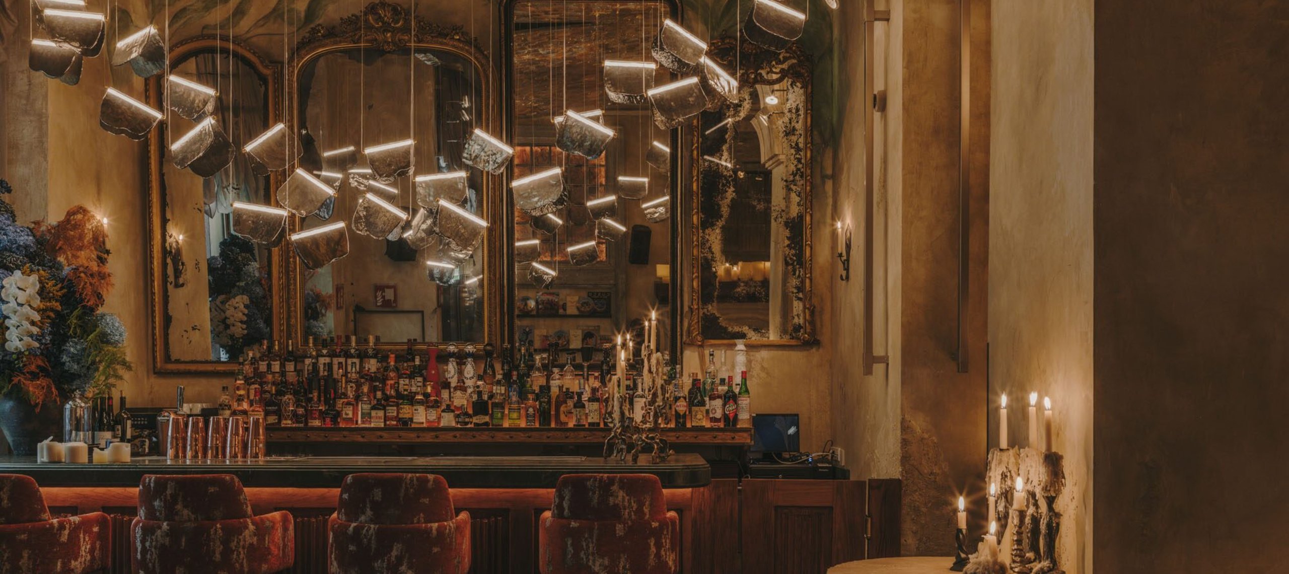 Interiorismo de restaurante y bar en Madrid: barra de 61 con lámparas escultóricas suspendidas, espejos dorados y taburetes de terciopelo · Archidom Studio