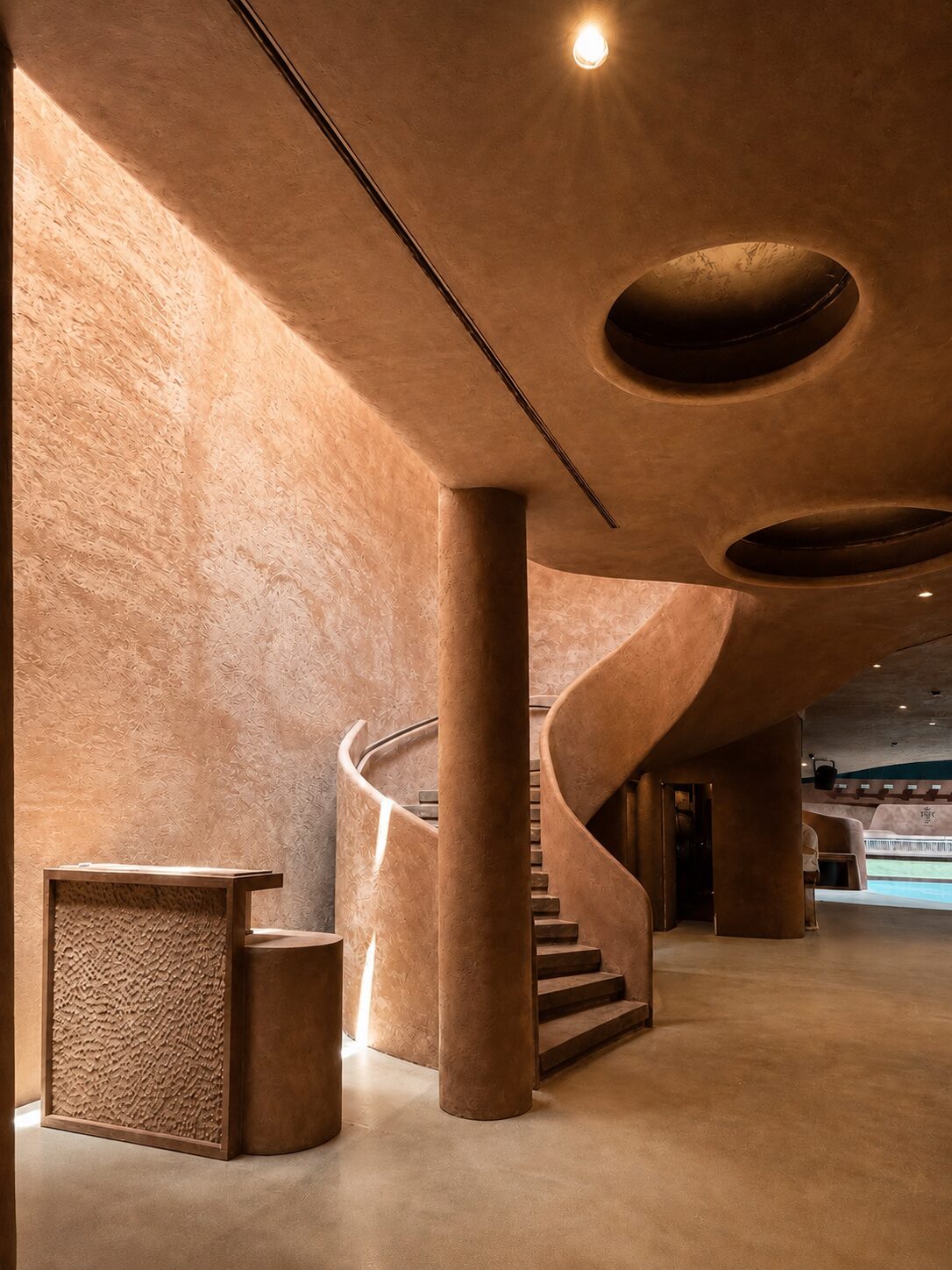 Bro Club entrance with a textured reception desk, cylindrical column and curved staircase beneath oval skylights