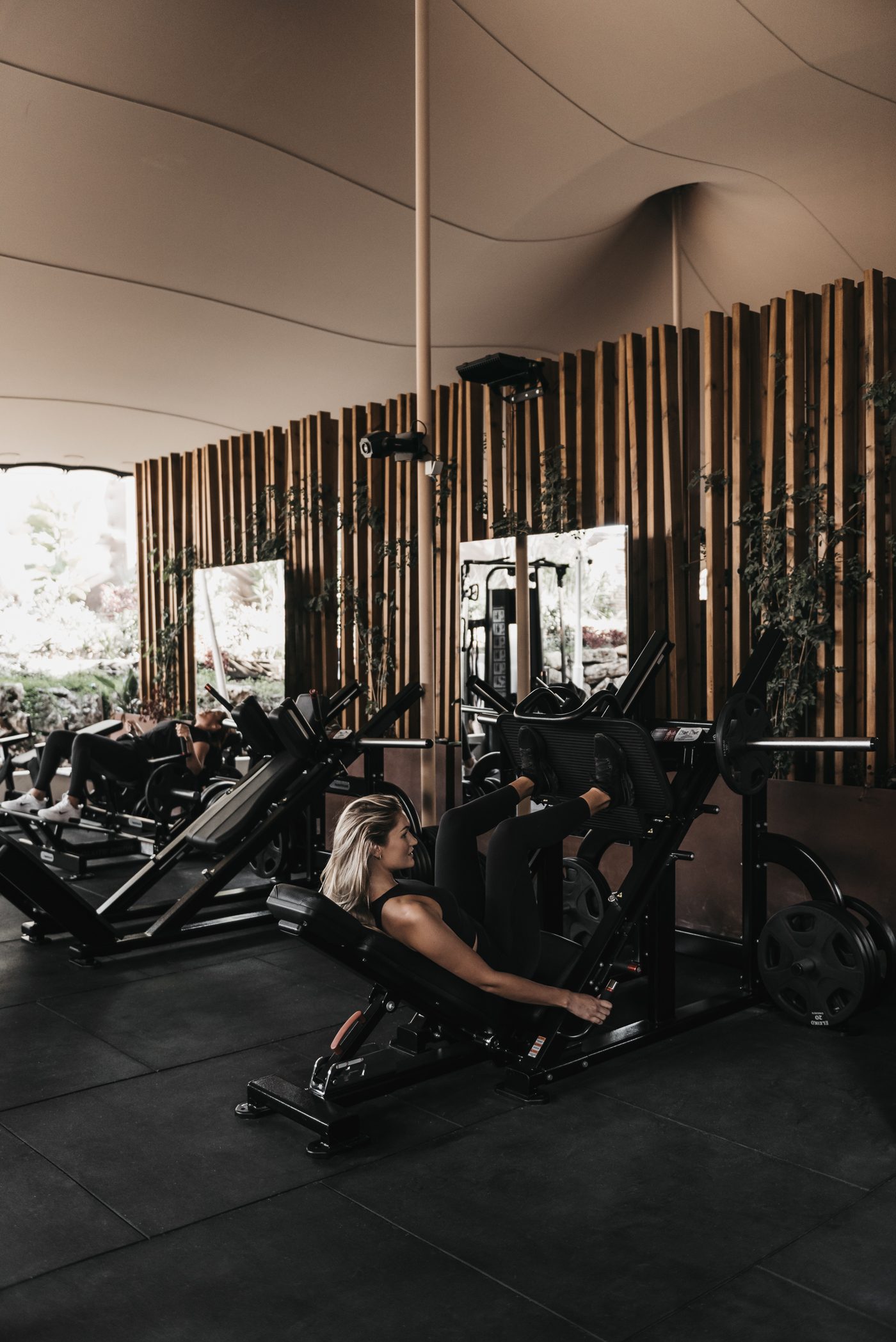 Gimnasio The I/O de NAC bajo cubierta textil, con máquinas de entrenamiento y muro de listones de madera con plantas