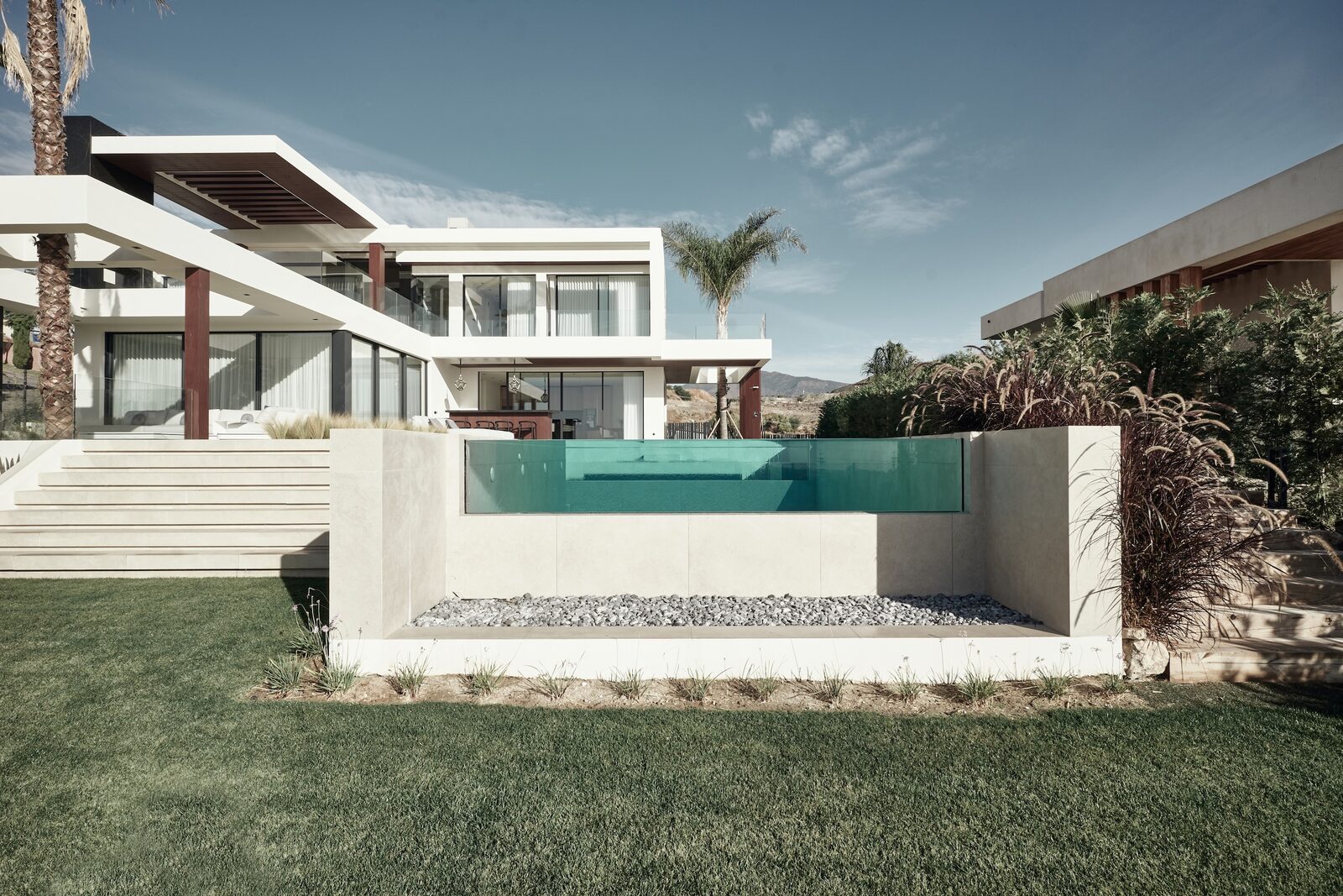 Villa Bond 09 草坪上方的玻璃立面泳池，后方为白色住宅与露台